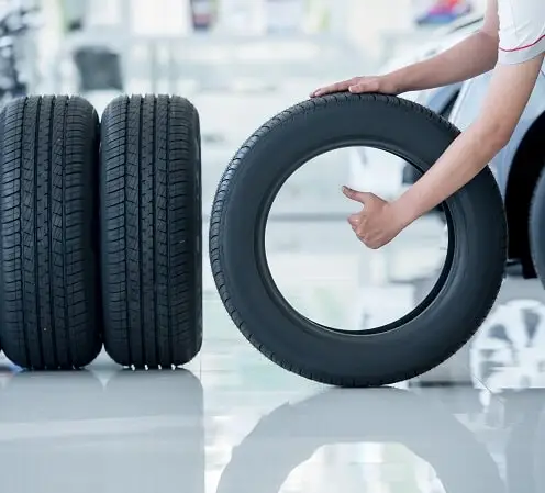 אדם אוחז בגלגל ולצד הגלגל שני גלגלים מונחים במאונך במוסך סופר צמיג ננהור