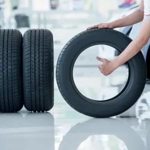 אדם אוחז בגלגל ולצד הגלגל שני גלגלים מונחים במאונך במוסך סופר צמיג ננהור